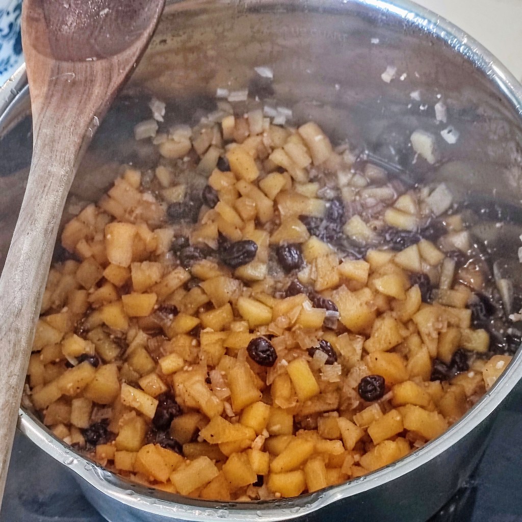 A pot of cooked diced apples mixed with raisins, with a wooden spoon resting on the side.